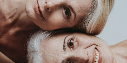 Two menopausal women smiling with their heads stacked on top of each other