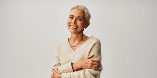 a menopausal woman holding herself and smiling against a grey background