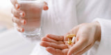 Someone holding a glass of water and a handful of supplements
