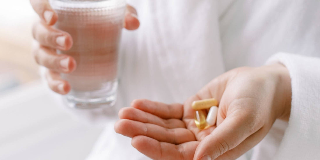 Someone holding a glass of water and a handful of supplements