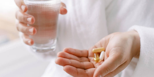 Someone holding a glass of water and a handful of supplements