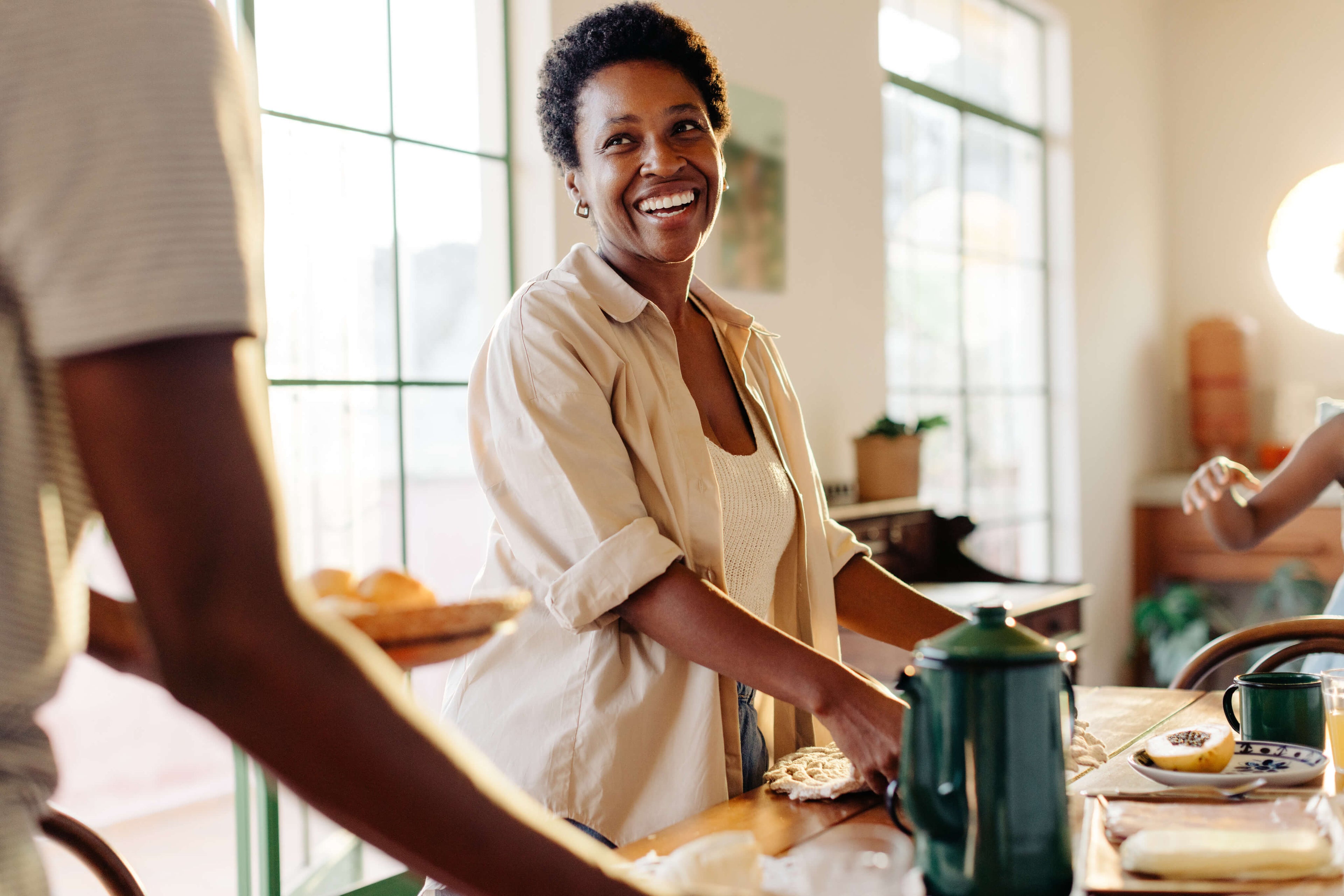Woman smiling at a table with a person partially visible, in a bright room.