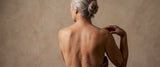 A menopausal women's bare back, against a neutral stone wall