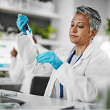A woman with grey hair working in a lab, depositing a green liquid into a test tube
