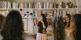 Woman taking a photo of a bookshelf filled with books and decorative items in a library.