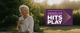 A smiling older woman in a white blouse sits outdoors in a garden setting, holding a mug. To her right is a purple promotional graphic with the text 'SÉRÉLYS HITS PLAY' and smaller white text above reading 'When discomfort puts life on pause.