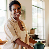 A darker skinned woman looking into the distance and smiling whilst in a neutral beige kitchen