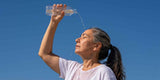 Woman pouring water from a bottle against a clear blue sky
