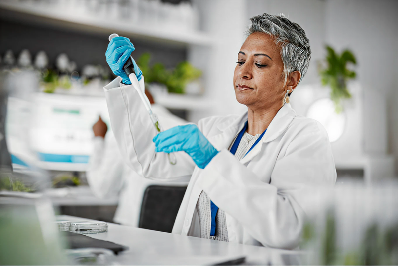 Scientist in a lab coat and gloves working with a pipette in a laboratory setting.