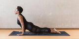 Woman practicing yoga in a black outfit on a wooden floor with a neutral wall background